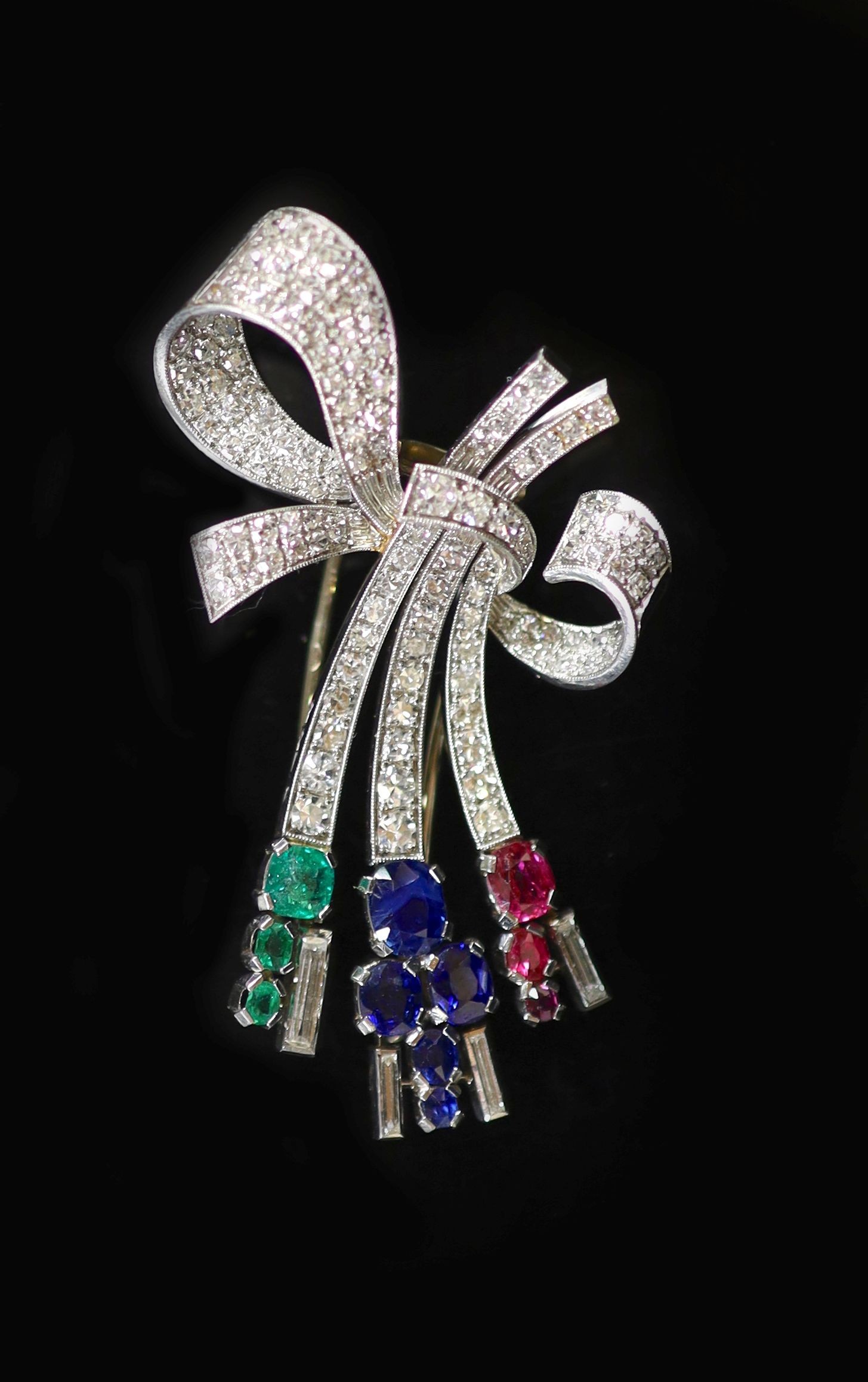 A mid 20th century Viennese platinum, ruby emerald, sapphire and diamond set stylised ribbon bow clip brooch